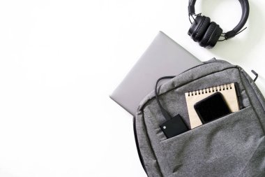 Laptop, akıllı telefon, not defteri, harici sssd ve beyaz arka planda kulaklık olan gri şehir sırt çantası. Cihazlarla yaşam tarzı konsepti. Modern öğrenci sırt çantası hariç.