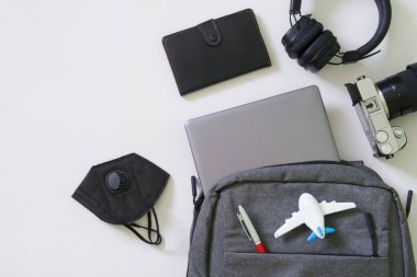 Sırt çantası ve cihazlar: laptop, kamera, kablosuz kulaklıklar ve koruyucu tıbbi maske - solunum cihazı. Yolculuk, hava yolculuğu ve Covid-19 salgını sırasında seyahat araçları konsepti. Yakın plan.