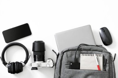 Gri sırt çantası ve beyaz arka planda bir sürü modern elektronik alet. Seyahat, gezi ve öğrenim aletleri konsepti. Bir fotoğrafçı ya da gezgin için sırt çantası konsepti. Duotone. Yakın plan.