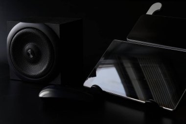 Siyah tablet, akıllı telefon, hoparlör ve bilgisayar faresi. Siyah arka plan. Siyah arka planda modern cihazların ve cihazların minimalist bir konsepti. Gün ışığı