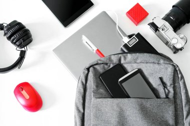 Laptop, akıllı telefon, cep telefonu, elektrik bankası, kulaklık, fare, kamera ve sırt çantası beyaz bir masada. Öğrenciler, gezginler ya da gazeteciler için hediyeler. Harici bir bataryadan şarj cihazları. Yakın plan.