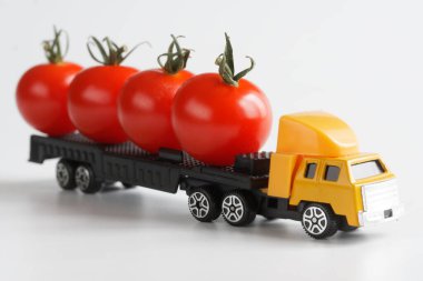 Taze kırmızı domates taşıyan bir karavanı olan oyuncak kamyon. Beyaz arka plan. Yeni hasattan büyük boy ürün ve sebze teslimatı konsepti. Oyuncak dünyası. Yakın plan.