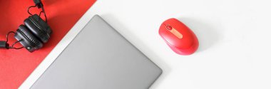 Gümüş-gri dizüstü bilgisayar ya da ultraviyole bilgisayar faresi ve kırmızı-beyaz arka planda siyah kulaklık. Gençler modern iş yeri konsepti. Bir yazı için boş yer. Web afişi. Gün ışığı