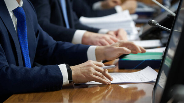 Hands of men - politicians, officials, businessmen or lawyers, sitting at a table with documents, microphones and monitors. Teamwork, negotiation or conference concept. Selective focusing. No face
