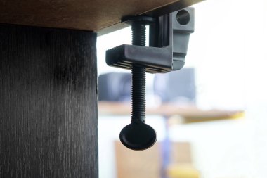 An example of attaching a clamp to a wooden surface of a table or workbench. Bottom view. Selective focusing. Free space for an inscription. Close-up