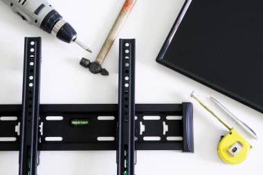 TV wall mount bracket, electric drill, fountain pen, tape measure, hammer and monitor on a white background. The concept of mounting a TV or computer monitor on a wall. Close-up