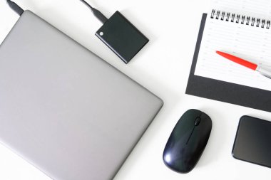 Silver laptop or ultrabook, computer mouse, pen, diary, portable ssd and smartphone on a white background. Concept of workplace, business planning and digital preservation. Close-up