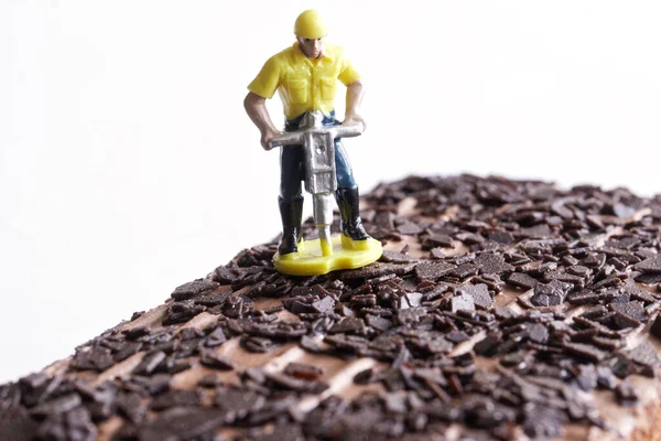 Figurine of a worker with a jackhammer stands on a biscuit cake sprinkled with crushed chocolate. The concept of making pastries and cakes, chocolate sprinkles. Selective focus. Macro. Close-up