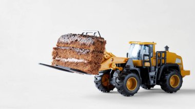 Oyuncak forklift bir parça çikolatalı bisküvi kek taşır. Bir pastane işletme kavramı, dev bir pastanenin hazırlanması ve taşınması. Beyaz arkaplan