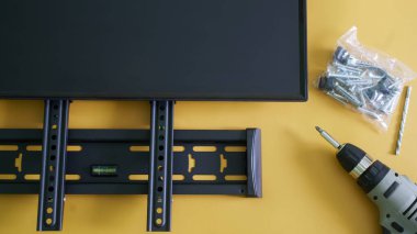 Bilgisayar monitörü, televizyon, tornavida, monte ve sarı arkaplanda monitör montajı için bileklik. İç mekanda bir bilgisayar monitörü ya da televizyon montajı kavramı. Yakın plan.