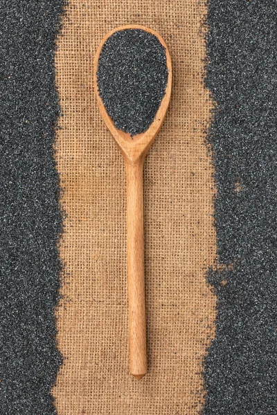 Wooden spoon with poppy seeds lying on sackcloth — Stock Photo, Image