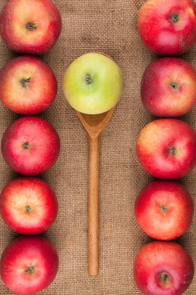 Spoon with green apple lying on the sackcloth among red apples — Stock Photo, Image