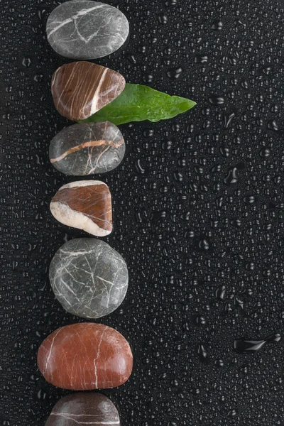 Striped stones and leaf lie on a wet black background — Stock Photo, Image