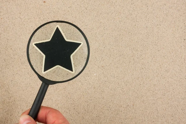 Hand with magnifying glass over the star, in the sand — Stock Photo, Image