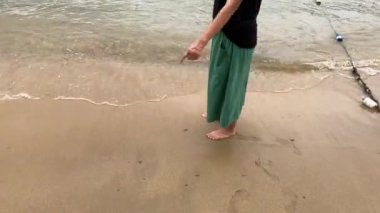 A woman walks slowly on the beach with the waves lapping her feet