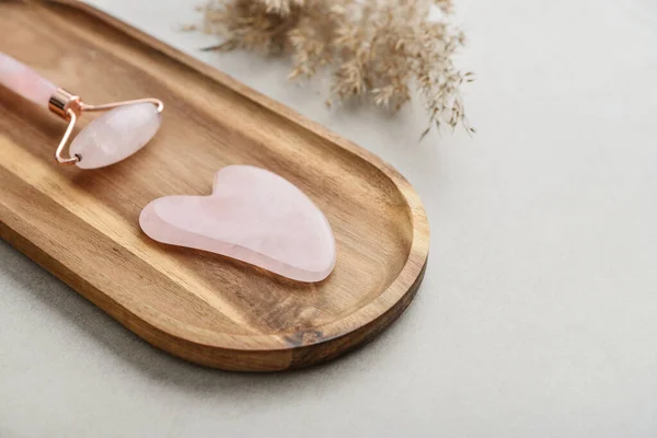 Facial rose quartz stone massage roller and gua sha massager made from natural stone on light concrete background, top view