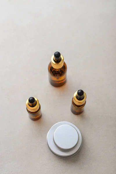 Dropper brown glass bottles, metal round tin cosmetic cans and small plastic can on light concrete background, top view