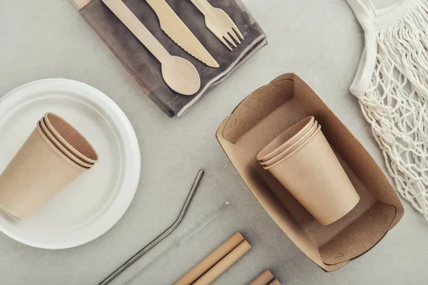 Set of eco-friendly tableware and kraft paper food packaging on light concrete background. Street food paper packaging - cups, plates, straws, containers and cutlery.