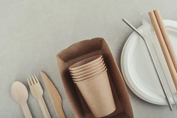 Set of eco-friendly tableware and kraft paper food packaging on light concrete background. Street food paper packaging - cups, plates, straws, containers and cutlery.
