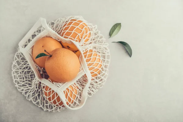 Cotton mesh bag with organic oranges on concrete background, top view