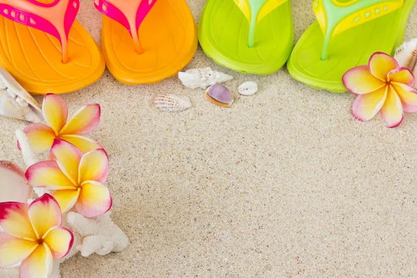 Flip flops i sanden med skal och frangipani blommor. Shopaholic — Stockfoto