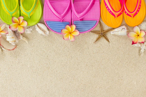 Chanclas de colores en la arena con conchas y harina de frangipani Imagen de stock