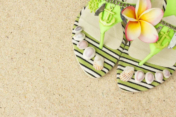 Sandalias, conchas marinas y frangipani sobre arena — Foto de Stock