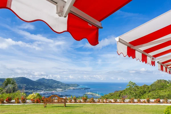 Toldo sobre o céu azul ensolarado brilhante com vista para o banco e o mar — Fotografia de Stock