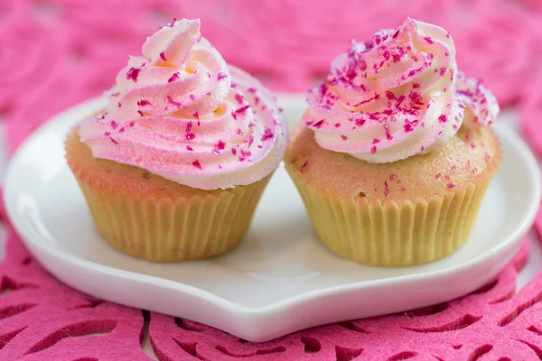 Two cupcake on white heart shaped plate, on pink background — Stock Photo, Image