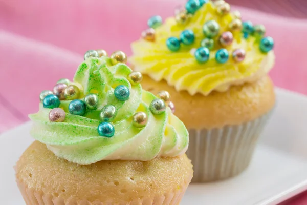 Dos cupcakes con crema de mantequilla amarilla y verde y colorido de — Foto de Stock