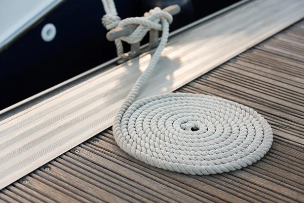 White rope coiled on a wooden dock and tied to a metal dock clea — Stock Photo, Image