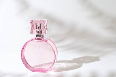 Beyaz arka planda, gölgeli ve kopyalama alanlı şeffaf pembe parfüm şişesi 