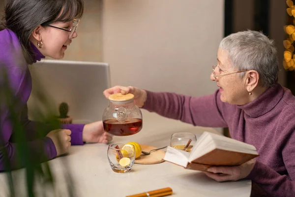 Büyükanne ve torun çay içer, masaya oturur ve kitap okurlar..