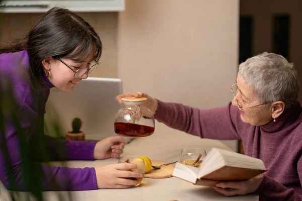 Bir büyükanne ve torun çay içer masada oturur ve kitap okurlar.. 