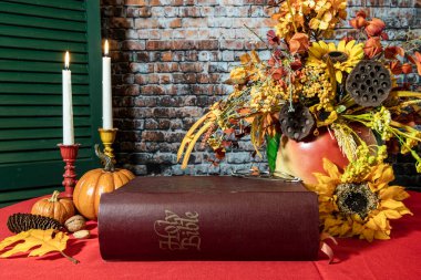 large bible on red with fall flowers pumpkins and burning candles in rustic setting
