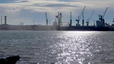 UKRAINE, CHERNOMORSK - 21 Şubat 2016: Liman vinçleri ve gemilerinin silüetleri, suyun arka planındaki ticaret limanında güneş ışığıyla parlıyor
