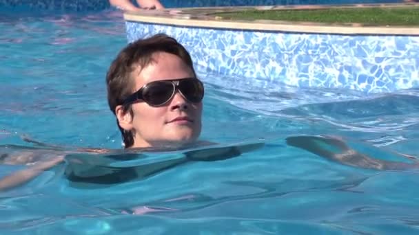 Chica flotando lentamente en el agua clara y azul de la piscina — Vídeos de Stock