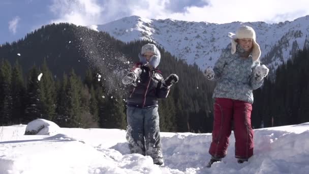 Vacaciones de invierno. Niños arrojaron bolas de nieve sobre un fondo de montañas cubiertas de nieve . — Vídeos de Stock