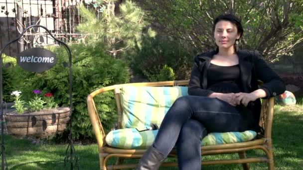 Giovane donna si siede su una panchina in un giardino — Video Stock