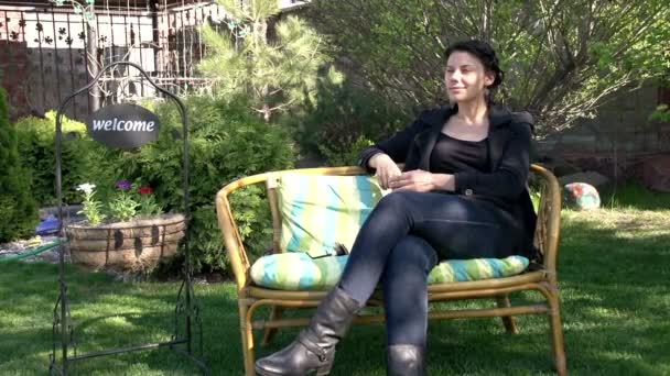 Jovem mulher senta-se em um banco em um jardim — Vídeo de Stock
