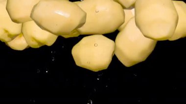 Black 'in üstüne atlayan soyulmuş patates. Üç çeşit taze soyulmuş ve yıkanmış patates yumrusu yukarı doğru uçuyor ve yavaşça siyah bir arka fonun üzerine düşüyor. Yavaş Hareket