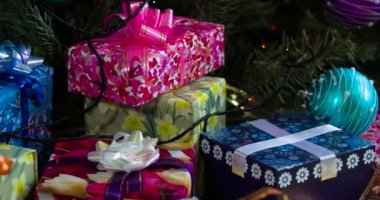 Renkli Noel akşamları. Kamera, parıltılı fiyonklarla süslenmiş hediye kutuları, Noel ağacı süslemeleri ve ışıltılı çelenklerle yavaşça hareket ediyor.