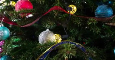 Parlayan Toplarla süslenmiş Noel Ağacı. Parlak parlak çelenklerle süslenmiş Noel ağacı dalları ve Noel süslemeleri kameranın önünde yavaşça hareket ediyor