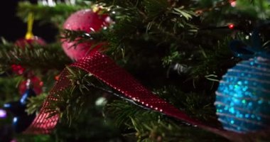 Dallardaki Noel Oyuncakları. Parlak parlak çelenklerle süslenmiş Noel ağacı dalları ve Noel süslemeleri kameranın önünde yavaşça hareket ediyor