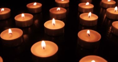 Bir sürü yanan mum. Kamera, zifiri karanlıkta yanan küçük mumlarla sahada yavaşça hareket ediyor. Havanın hareketleriyle hareket eden alevler