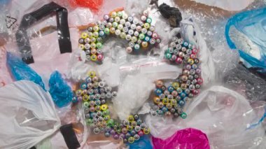 Geri Dönüşüm İçin Plastik Paket Toplama. HD döngüsü. Geri dönüşüm sembolü eski AA pillerden oluşuyor. Renkli plastik torbalar arasında yavaşça döner ve koleksiyonu, geri dönüşümü ve yeniden kullanımını sembolize eder