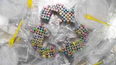 Geri dönüşüm için plastik kap koleksiyonu. Geri dönüşüm sembolü eski AA pillerden oluşuyor. Koleksiyonu, geri dönüşümü ve yeniden kullanımını sembolize etmek için yavaş yavaş plastik ambalajlar ve ev kimyasalları ve gıda maddelerinin konteynerleri arasında döner.