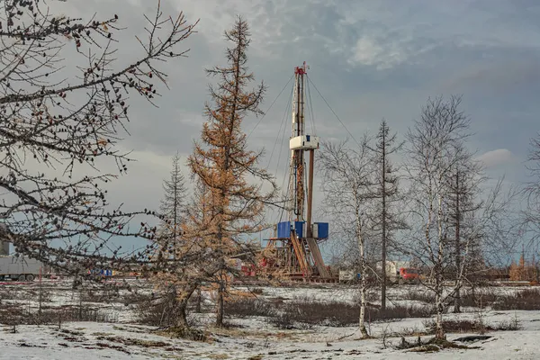 Winter landscape of an oil and gas field with a drilling rig and special equipment in the polar forest tundra. Ground is covered with snow