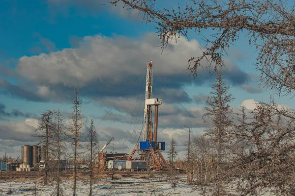 Winter landscape of an oil and gas field with a drilling rig and special equipment in the polar forest tundra. Ground is covered with snow