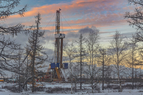Winter landscape of an oil and gas field with a drilling rig and special equipment in the polar forest tundra. Ground is covered with snow